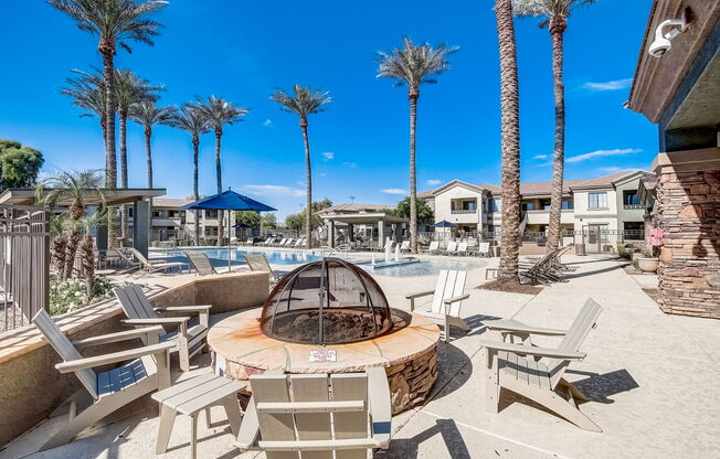 a fire pit with chairs around it near a pool with palm trees at Adiamo Palm Valley, Goodyear, AZ