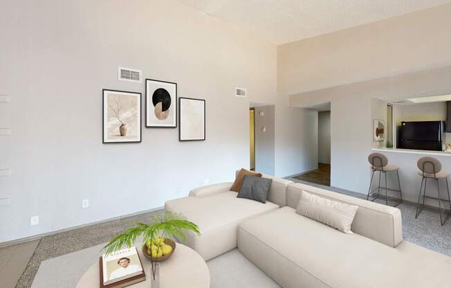 A living room with a white couch, a coffee table with a book and a plant on it, and a wall with three framed pictures.