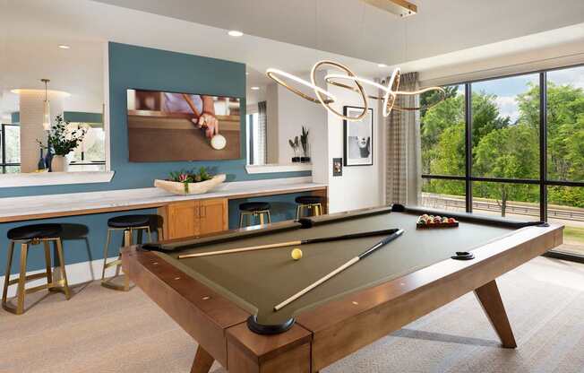 A pool table is in the middle of a room with a bar and a window.