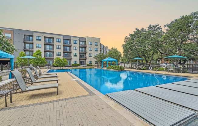 a swimming pool with chairs and umbrellas in front of an apartment building