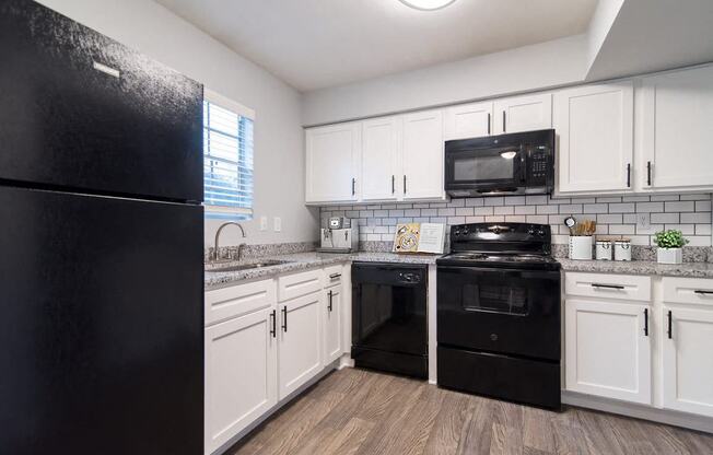 A black refrigerator stands next to a kitchen counter with white cabinets and a black oven.
