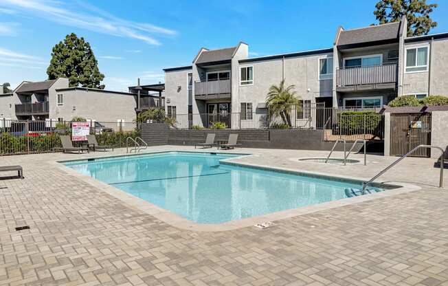 A swimming pool surrounded by a brick patio and apartment buildings.