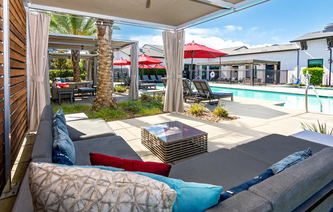A patio with a couch, pillows, and a pool in the background.