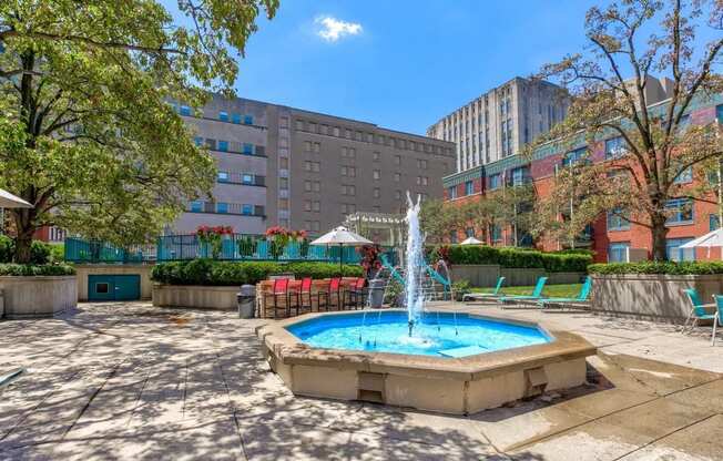 a fountain in the middle of a park with buildings in the background