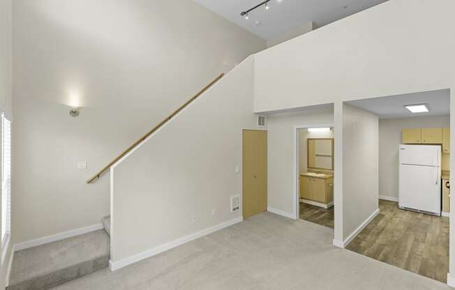 Loft-Style Apartment with Sconce Lighting Up Stairs to Living Area, Plush Carpeting, and Kitchen View in the Background at Sir Gallahad Apartment Homes, Bellevue