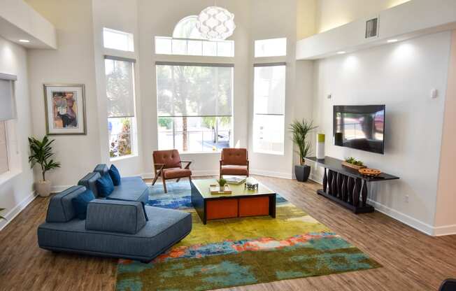 Clubhouse seating area with navy blue sofas, Coffee table, and mounted television on wall.  large picture windows providing a natural light within the room