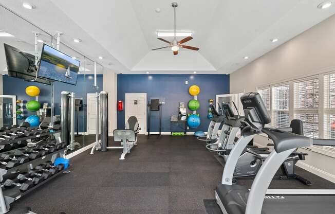 a gym with cardio machines and weights and a ceiling fan