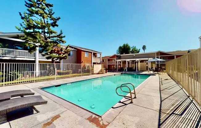 A swimming pool surrounded by a fence and lunge chairs and umbrella.