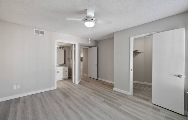 A spacious room with a ceiling fan and light, hardwood floors, and white walls.