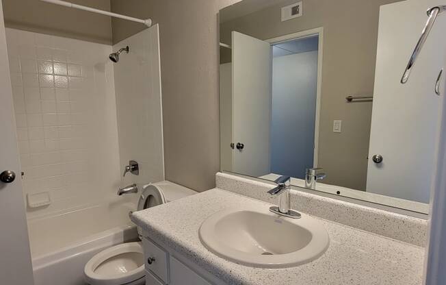 Shared bathroom with white fixtures and vanity cabinets at La Mesa Village Apartments in La Mesa, California.