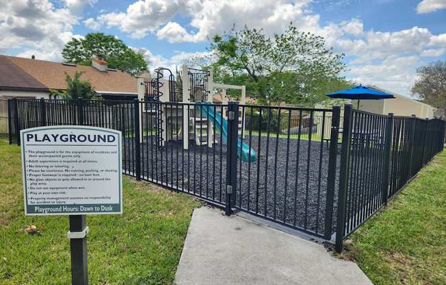 A sign on a playground gate provides information about the playground's rules and regulations.