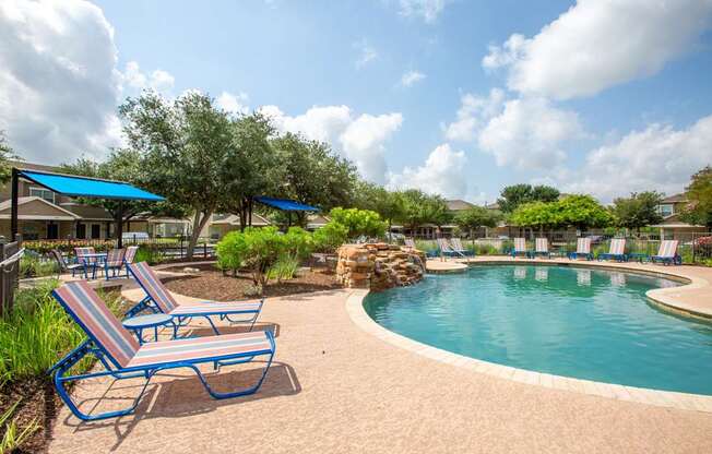 A pool with a blue umbrella and a bench.