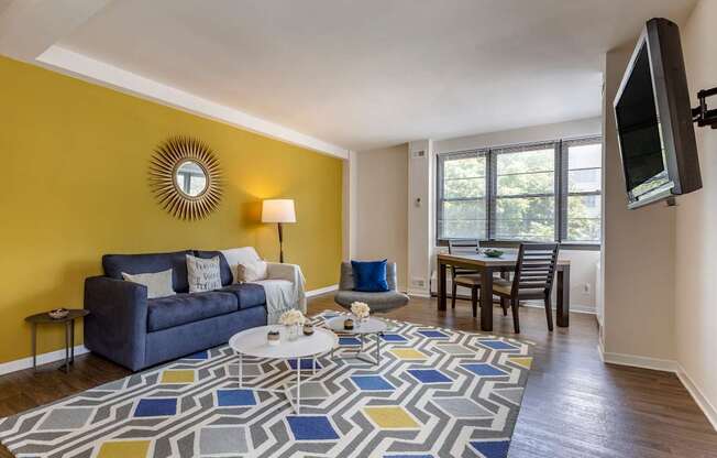 A living room with a blue couch, a white coffee table, and a flat screen TV mounted on the wall.