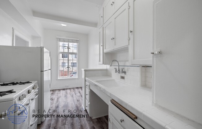 a white kitchen with white cabinets and a stove and a window