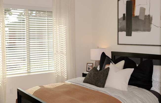 A bed with a brown comforter and pillows in front of a window with blinds.