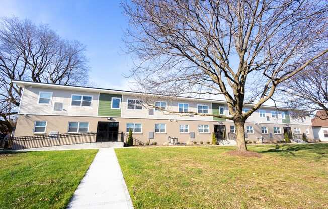 the exterior of an apartment building with a sidewalk and a tree