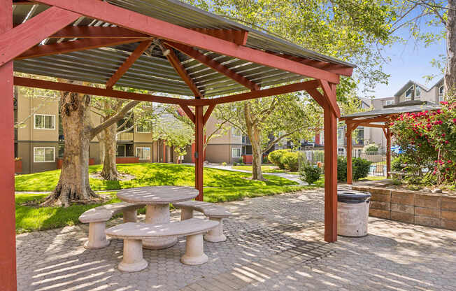 A red and white pavilion with a picnic table in the middle of a brick patio.