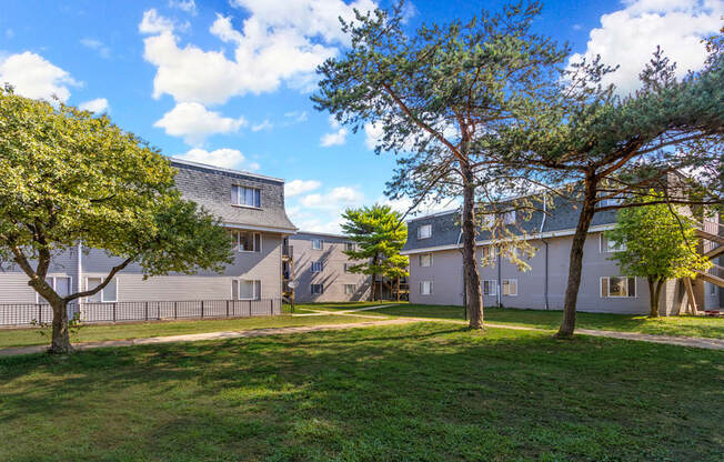 A sunny day at a grassy park with trees and apartment buildings in the background.