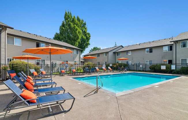 A pool area with sun loungers and umbrellas in front of apartment buildings.