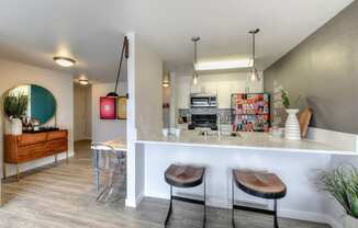 Kitchen and Bar Seating with Hardwood Inspired Floor, Decorated Refrigerator, and "A Man Walks Into a Bar" Painted on the Wall