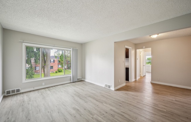 A spacious room with wooden floors and a large window overlooking a residential area.