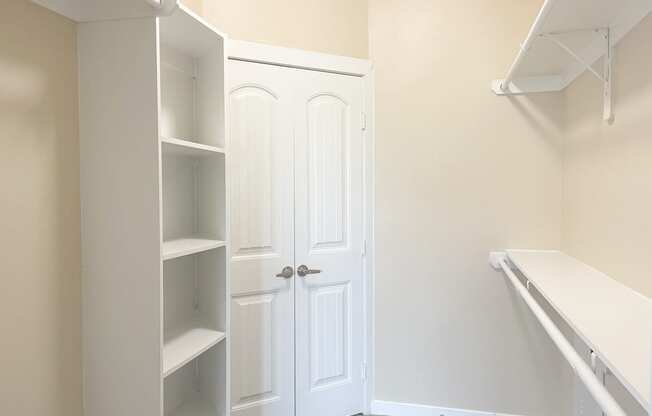 a walk in closet with a white closet door and white shelves