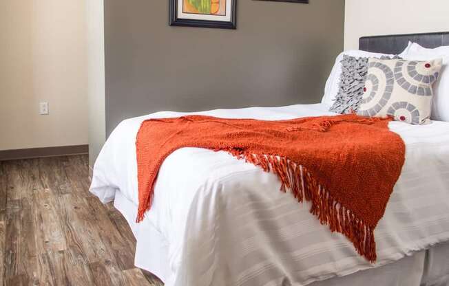 A bed with a white comforter and a red throw blanket.