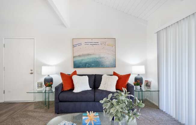 a living room with white walls and a dark blue couch with orange and white pillows
