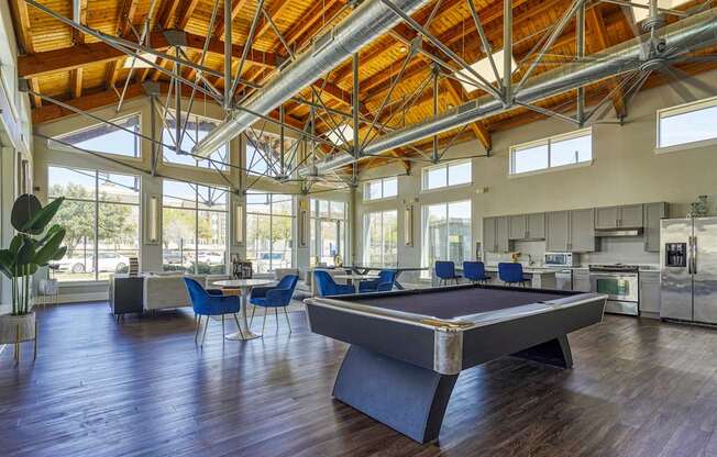 A billiard table is in the middle of a room with a high ceiling and lots of windows.