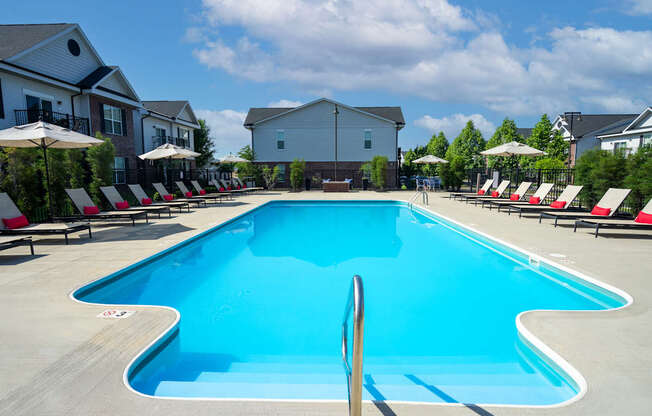 A large blue swimming pool surrounded by red lounge chairs and umbrellas.