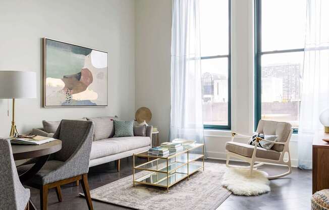 A modern living room with a grey sofa, a wooden dining table and chairs, a rug, and a painting on the wall at The Pennsylvanian Apartments, Pittsburgh, 15222