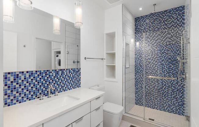 A bathroom with a blue tiled shower and white countertop.