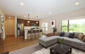 Eagan, MN Glen Pond Addition Apartment. A living room with a couch, coffee table, and large window with a kitchen in the background.