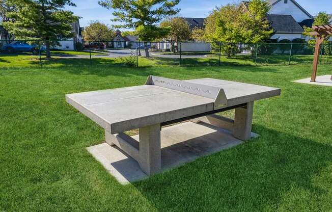 A concrete table in a grassy area with a house in the background.