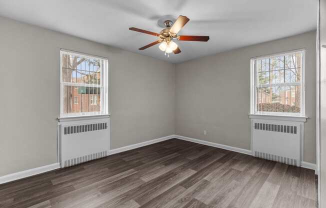 an empty living room with two windows and a ceiling fan