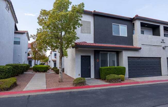 A tree in front of a grey house with a black garage door.