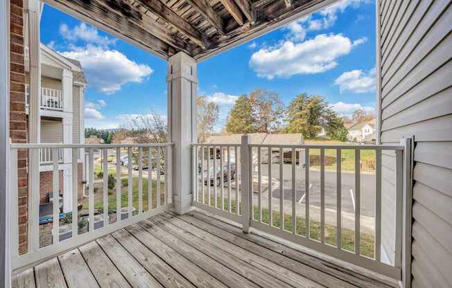 A balcony with a white railing and wooden floor overlooks a parking lot.