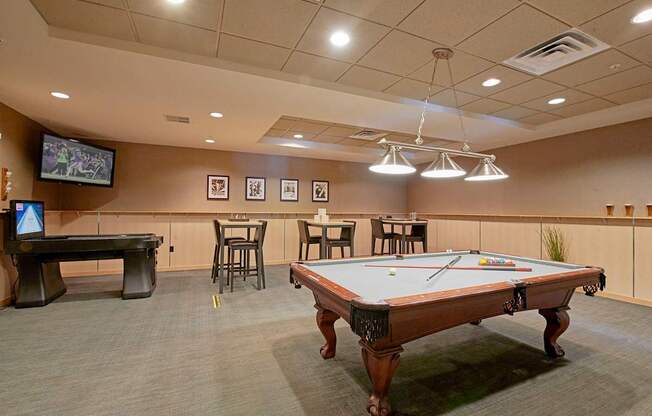 A pool table in the middle of a room with a TV and tables.