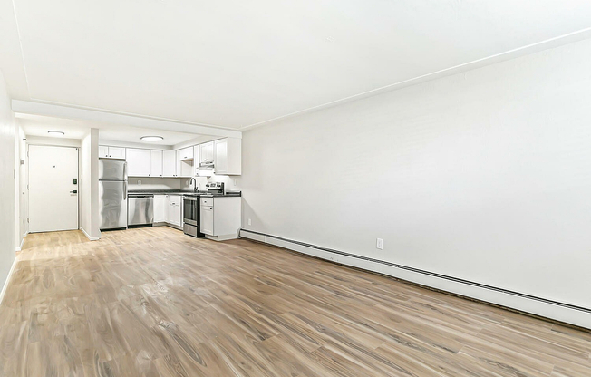 Bright, spacious open-concept apartment with sleek hardwood floors and a modern kitchen featuring stainless steel appliances and elegant white cabinetry.