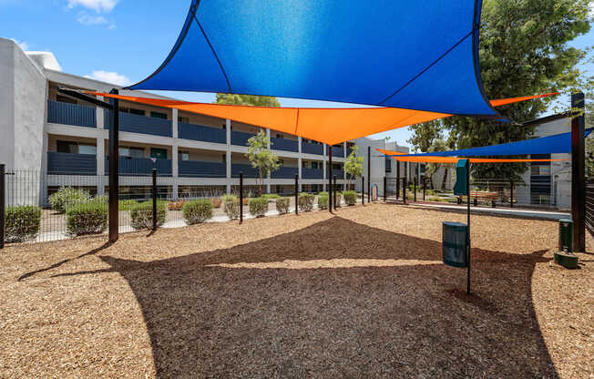 A playground with a blue and orange shade structure.