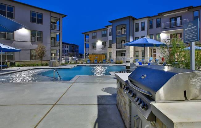 a grilling station next to a swimming pool with an apartment building in the background