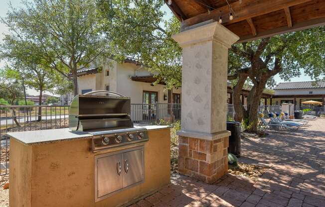 A brick pillar stands next to a stove in a sunny outdoor area.