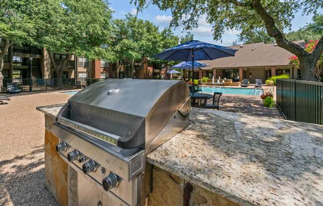 an outdoor kitchen with a grill and a swimming pool in the background