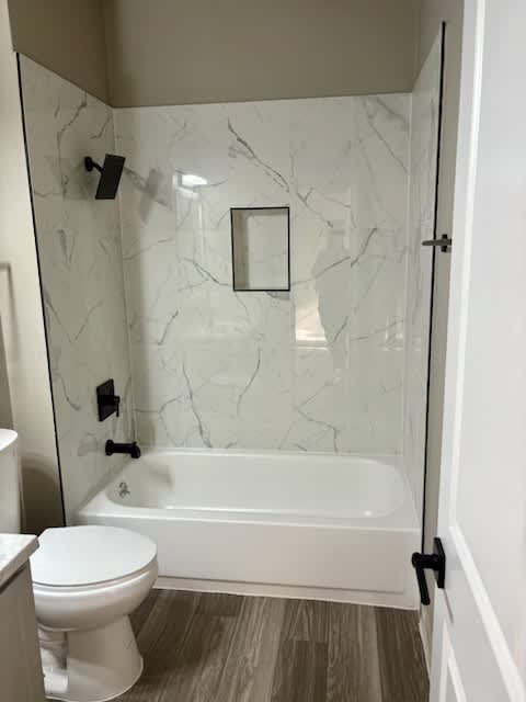 A white toilet sits in a bathroom with a marble wall and a white tub.