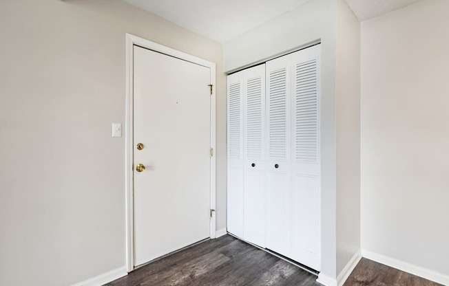 A white door with a gold handle is on the left and a white closet with white doors is on the right.