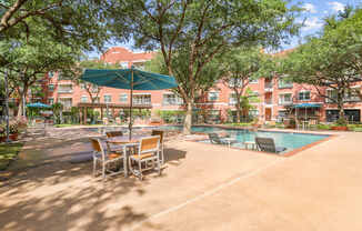 A pool area with a table and chairs and a green umbrella.