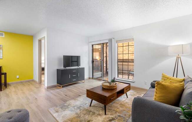 A living room with a grey couch, a wooden coffee table, and a yellow accent wall.