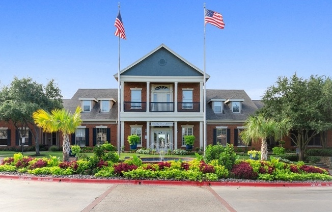 Clubhouse entrance exterior, two USA flagpoles, landscape flower bed with fountain and driveway