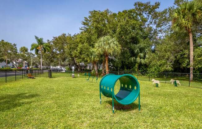 a green seesaw in a park with trees