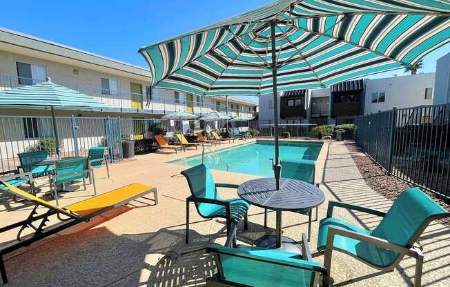 A sunny day at the pool with a striped umbrella providing shade.